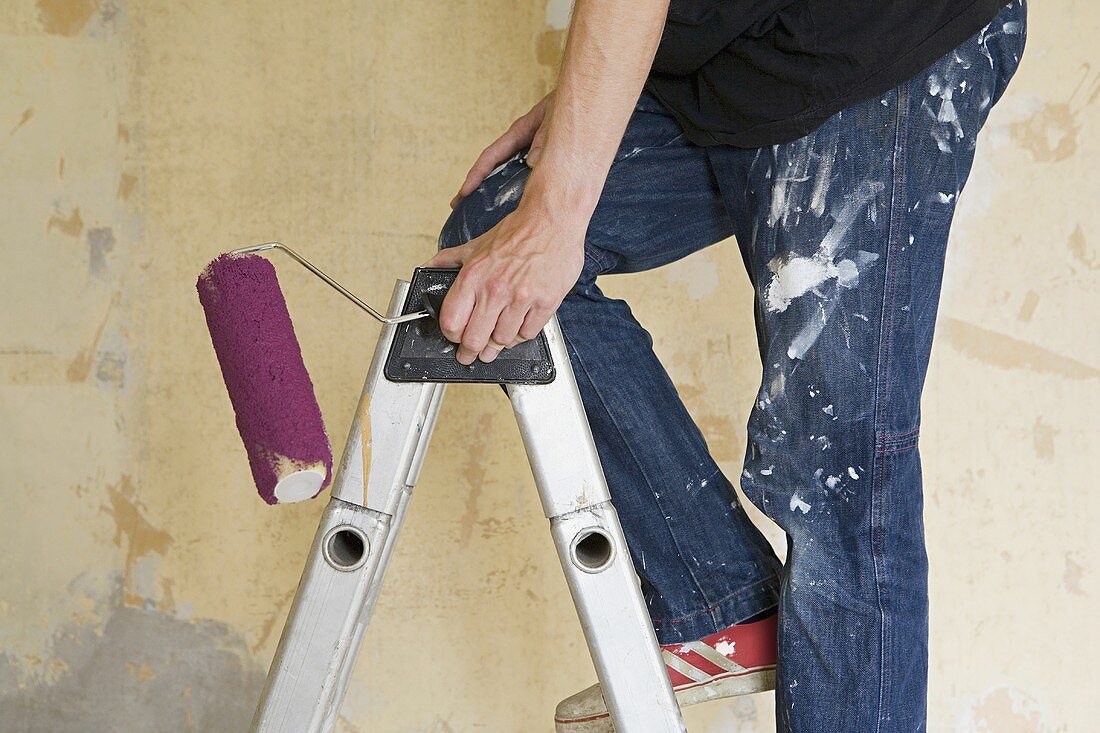 A man on a stepladder with a paint roller