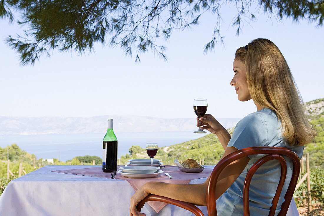 Frau sitzt mit Rotwein am Tisch mit Ausblick auf einen See