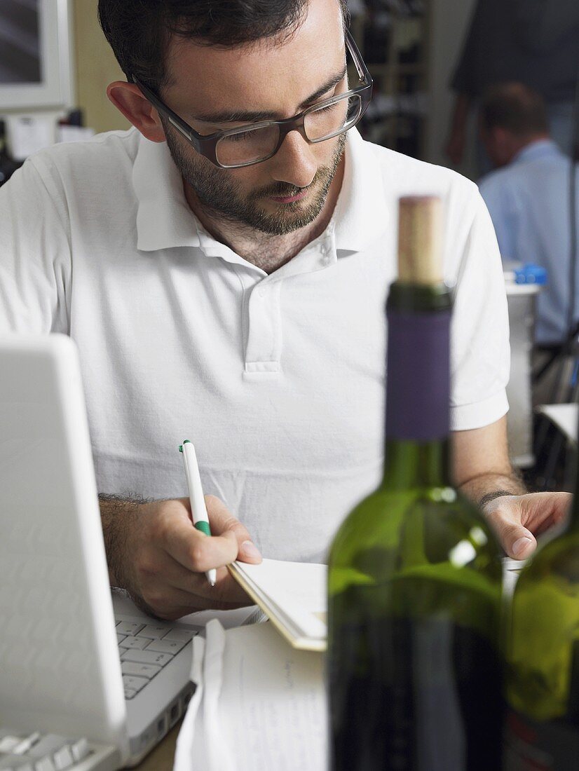 A man using a laptop computer with a bottle of wine in the foreground