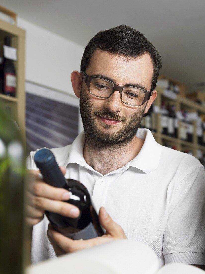 A bearded man with glasses looking at a bottle of wine
