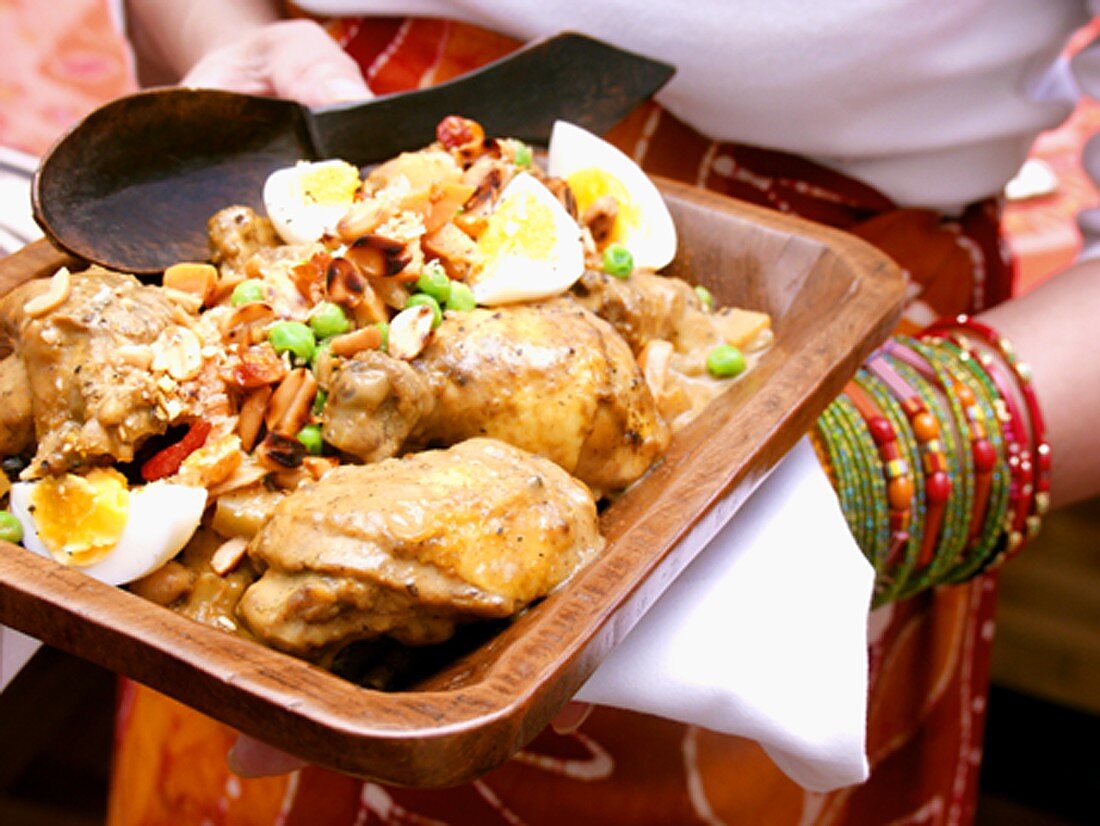 African woman holding bowl of chicken with peanuts & egg