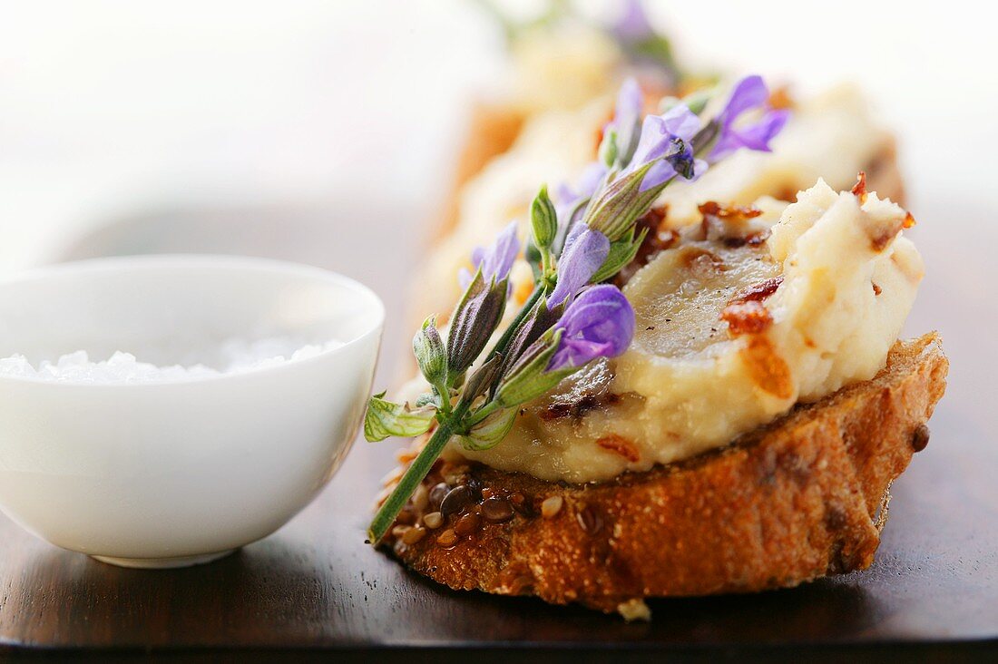 Geröstetes Brot mit Bohnenpaste, Speck und Blüten; Salz