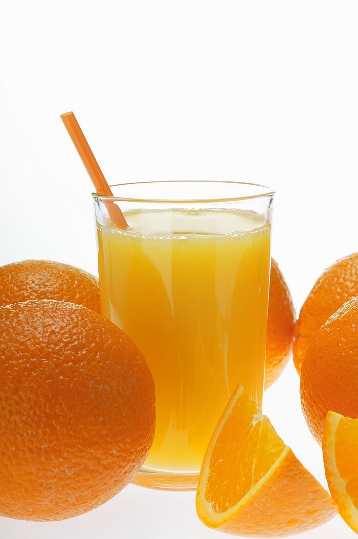 Orangensaft im Glas mit Strohhalm zwischen Orangen
