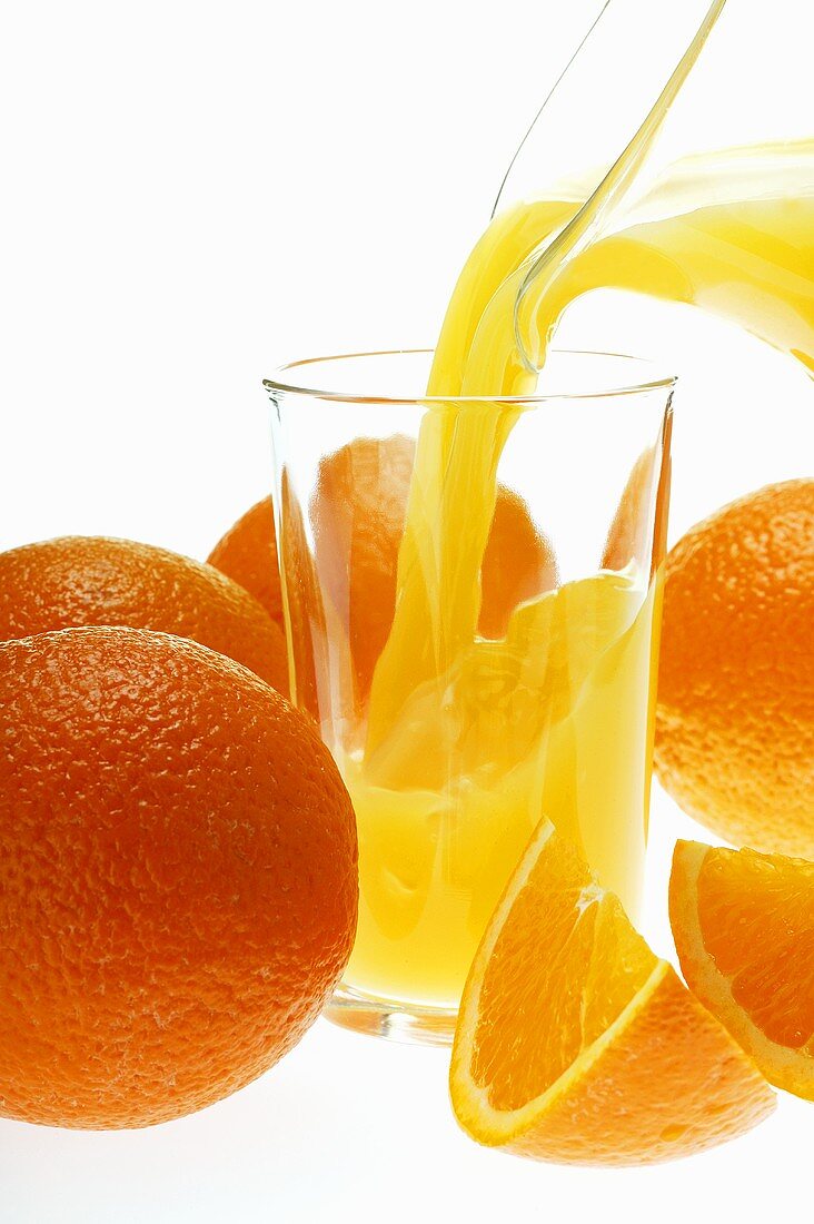Orangensaft in Glas einschenken zwischen Orangen