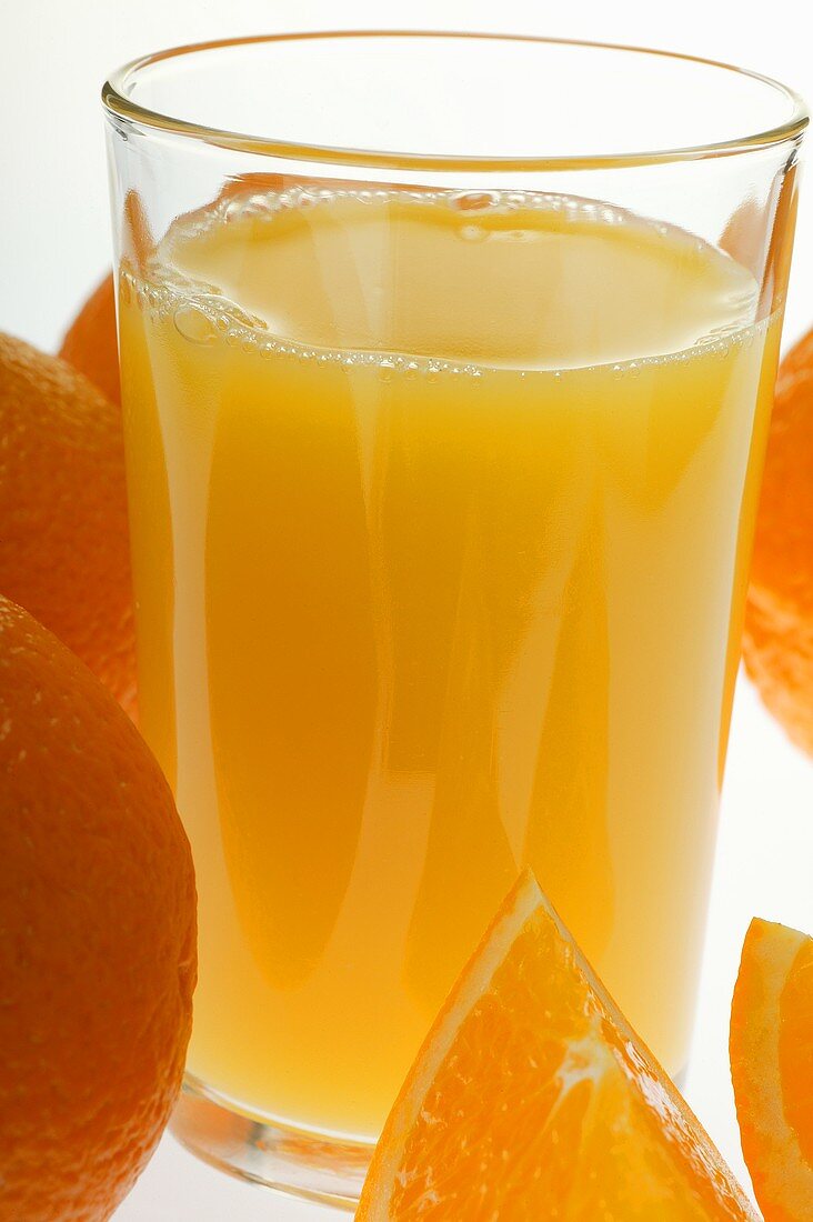 Orange juice in glass among oranges (close-up)