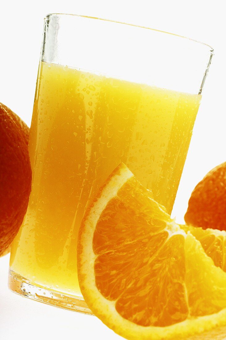 Orange juice in glass among oranges