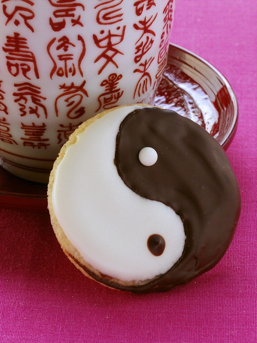 A Yin Yang biscuit beside a Chinese cup