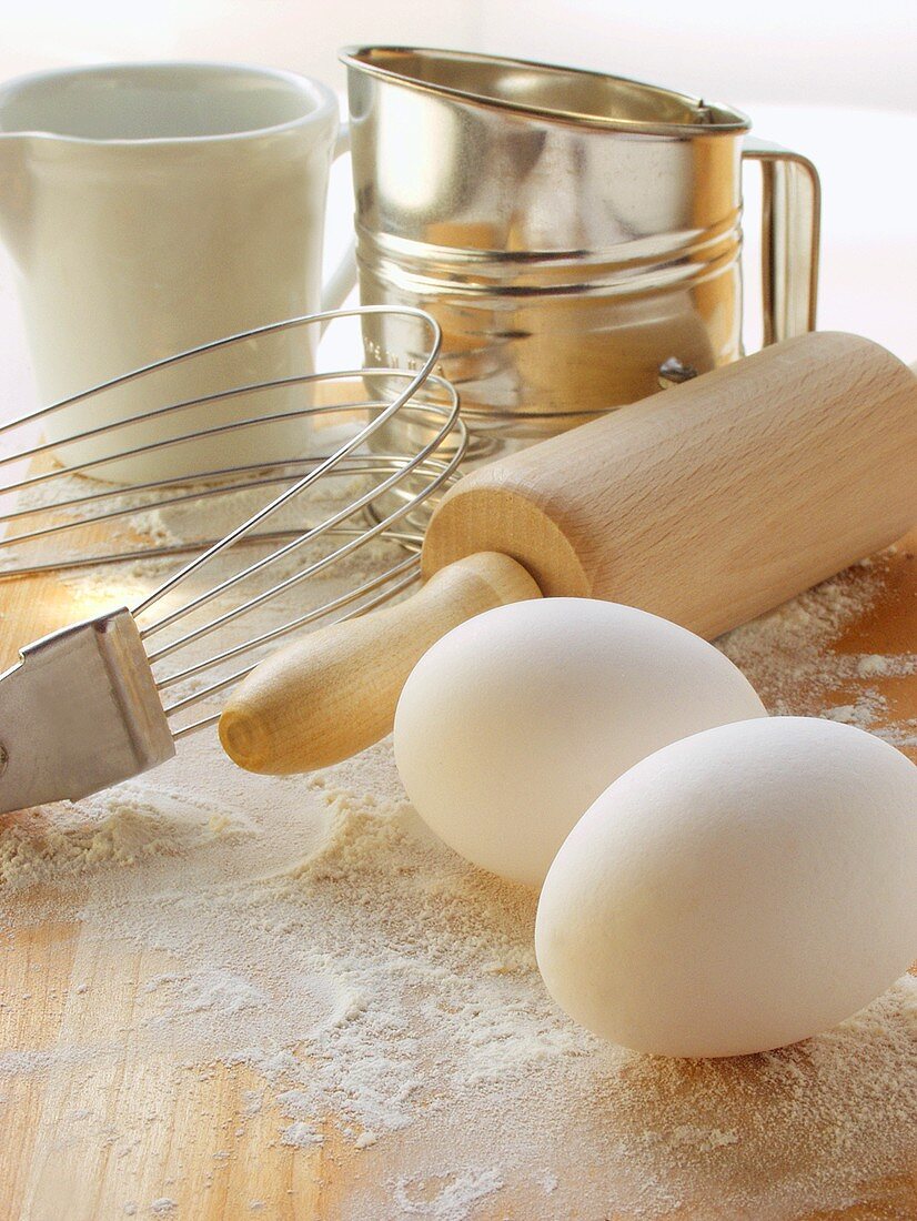 Various baking utensils, eggs and flour on chopping board