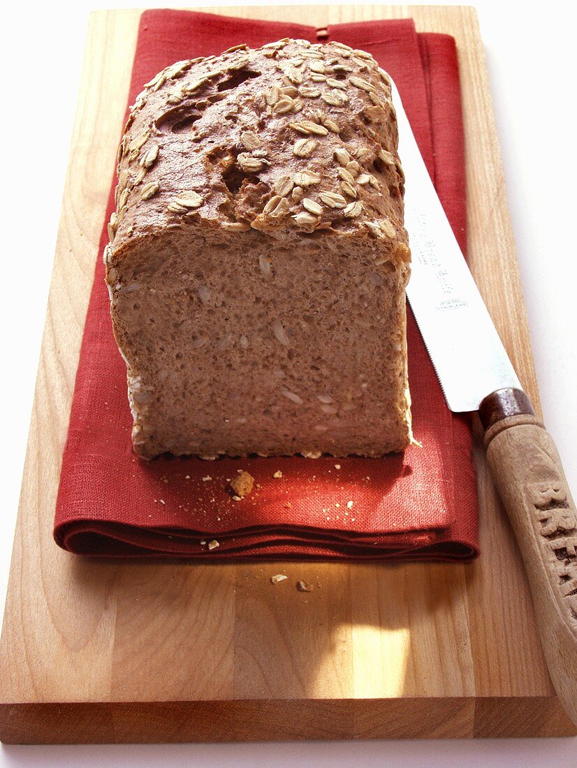 Wholemeal bread with oat flakes on red napkin; knife