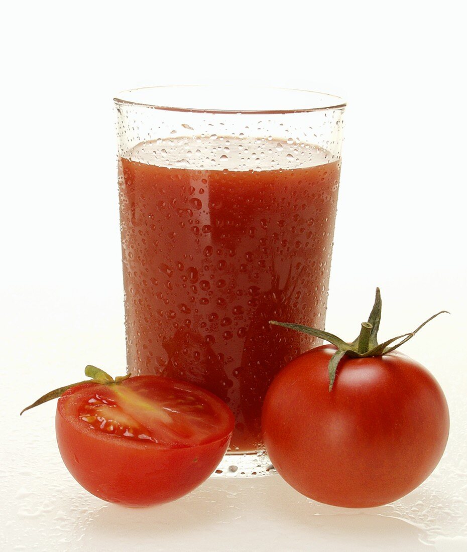 Tomatensaft im Glas mit Wassertropfen; ganze und halbe Tomate