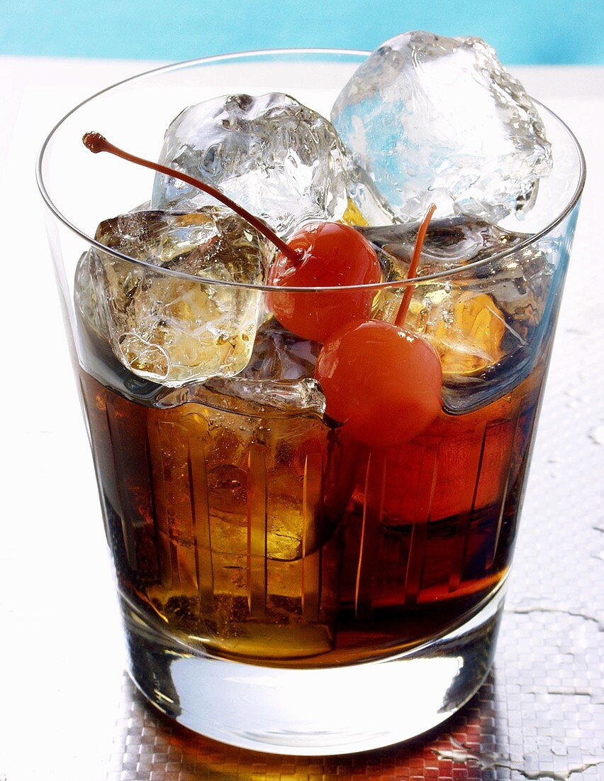 Drink with rum, ice cubes and cocktail cherries