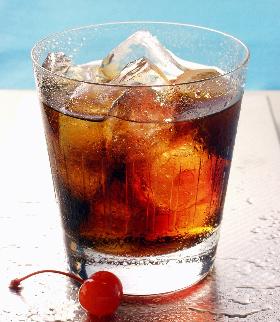 Drink mit Rum, Orange und Eiswürfeln; Cocktailkirsche