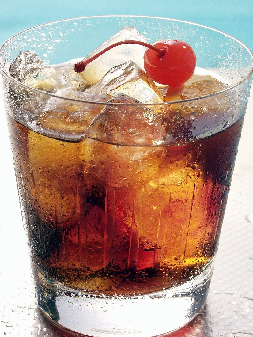 Drink mit Rum, Orange, Eiswürfeln und Cocktailkirsche