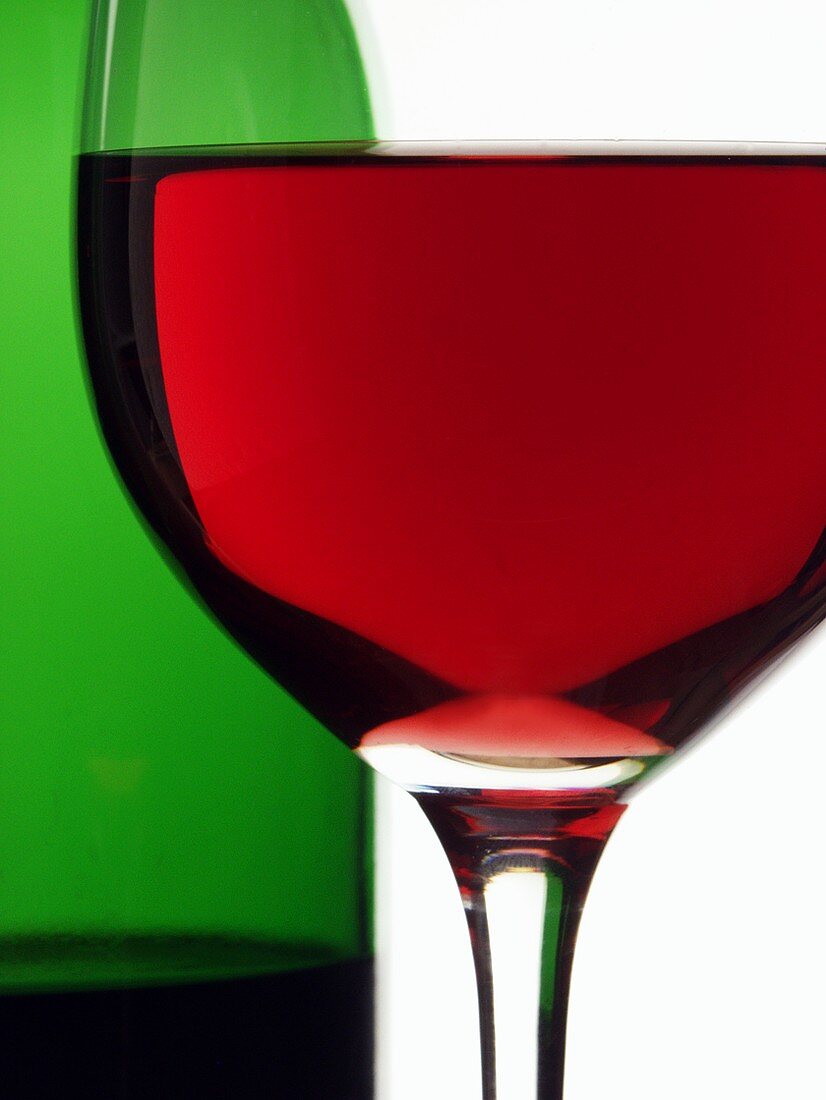 Red wine glass in front of red wine bottle (close-up)