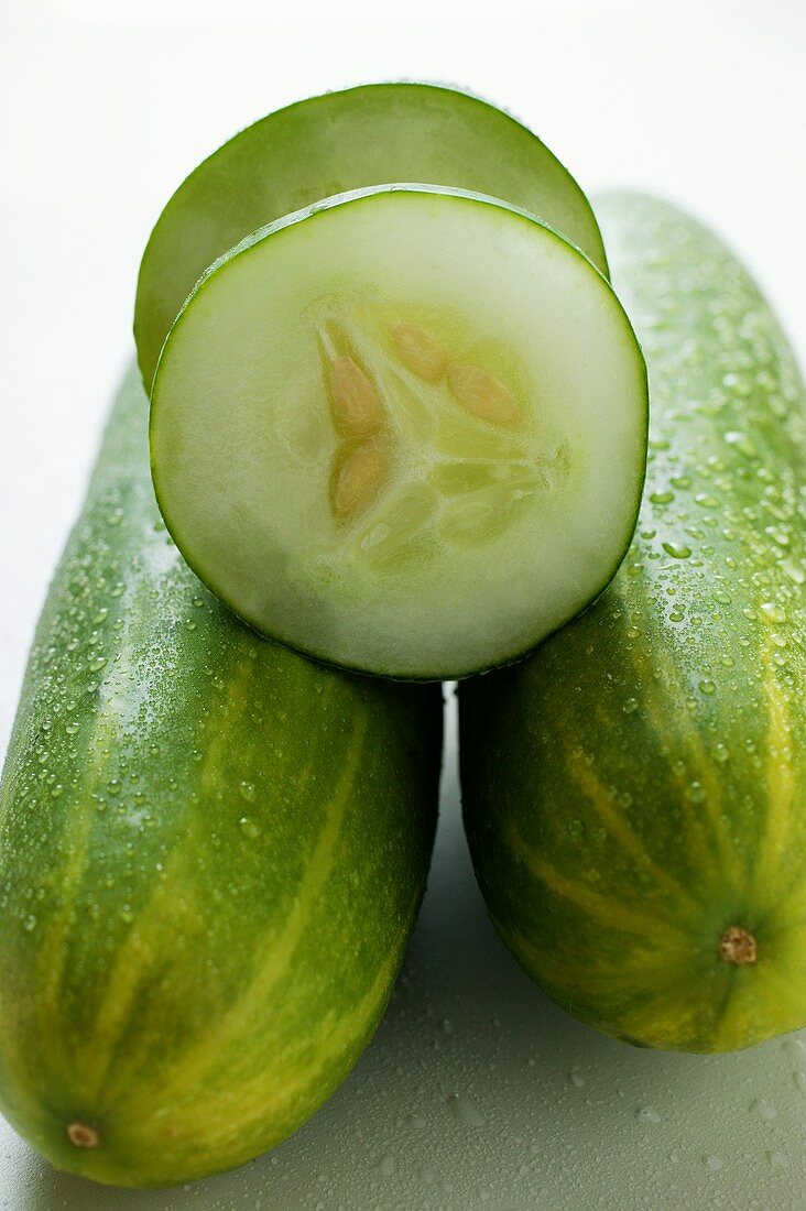 Fresh cucumbers with drops of water, one with a piece cut off