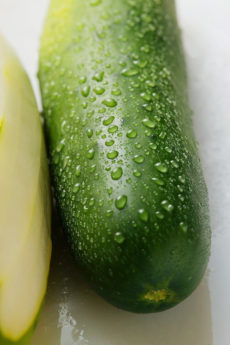 Two cucumbers with drops of water, one peeled