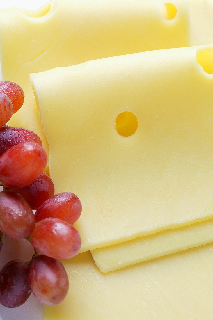 Emmental cheese in slices with red grapes (close-up)