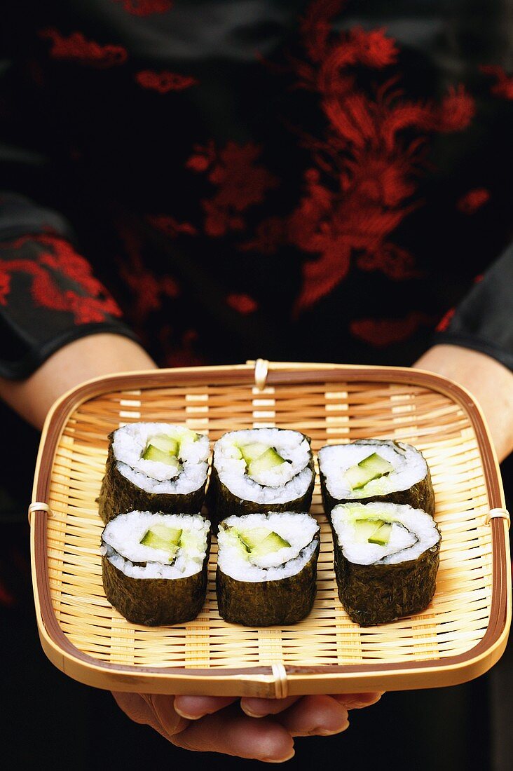 Asian woman holding maki-sushi on wicker tray