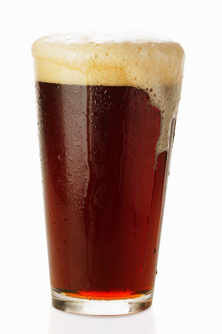 Dark beer in glass, frothing over