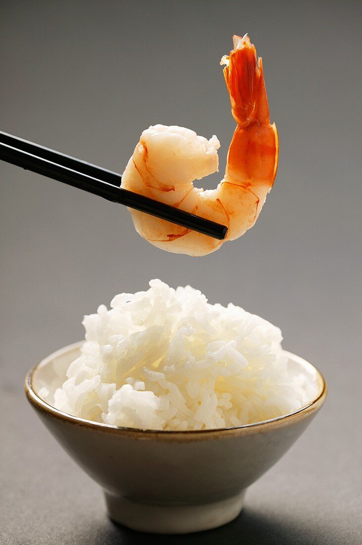 Shrimp on chopsticks above bowl of rice