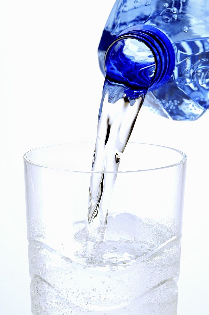 Wasser wird aus blauer Flasche in ein Glas gegossen