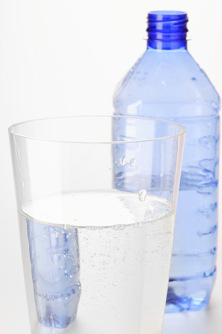 Mineral water in glass in front of plastic bottle