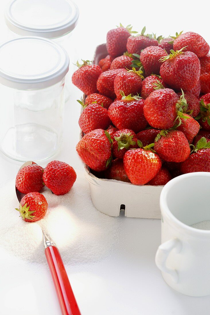 Frische Erdbeeren in Pappschale, Zucker und Einmachgläser