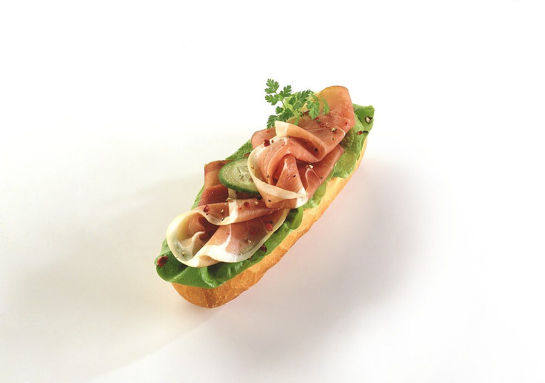 Baguette topped with raw ham, lettuce and cucumber