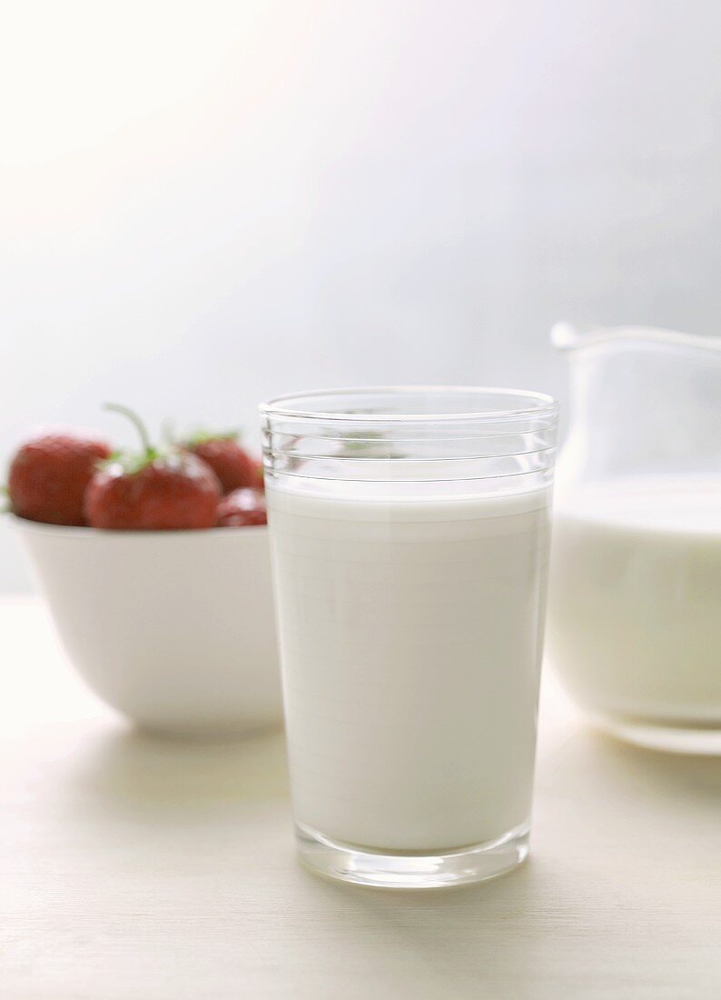 Glass of milk and milk jug; strawberries in white bowl