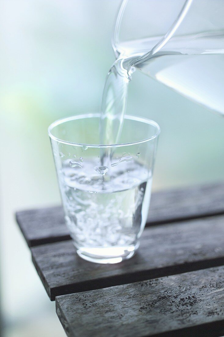 Wasser aus Glaskrug in Glas gießen