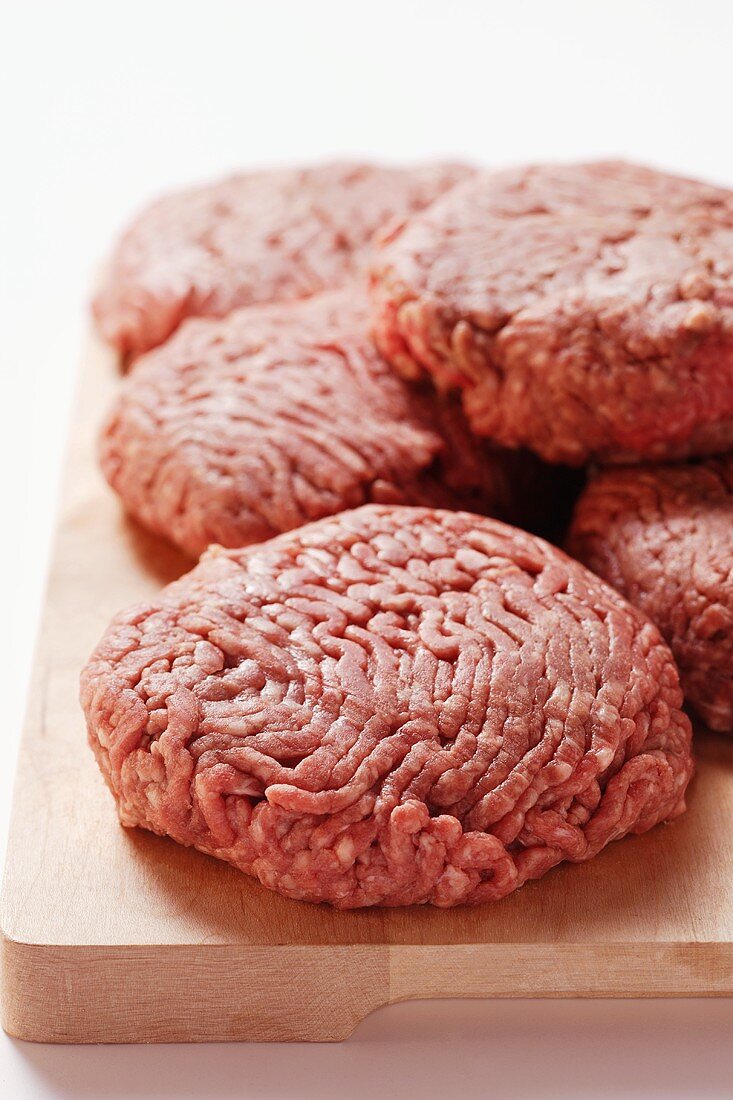 Raw burgers on wooden chopping board