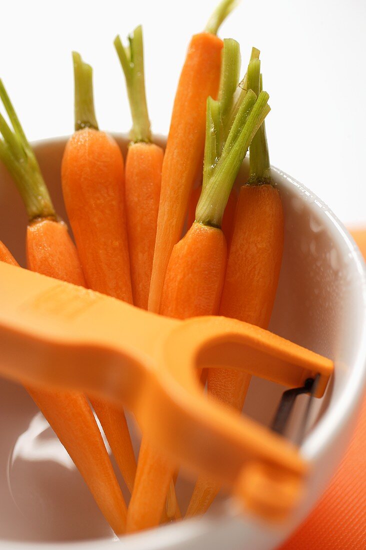 Peeled carrots in white cup with peeler