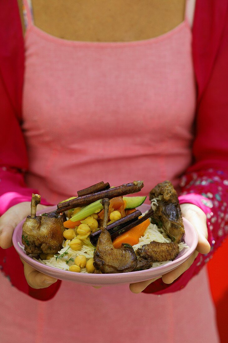 Frau serviert gebratene Taube mit Gemüse auf Nudeln (Marokko)