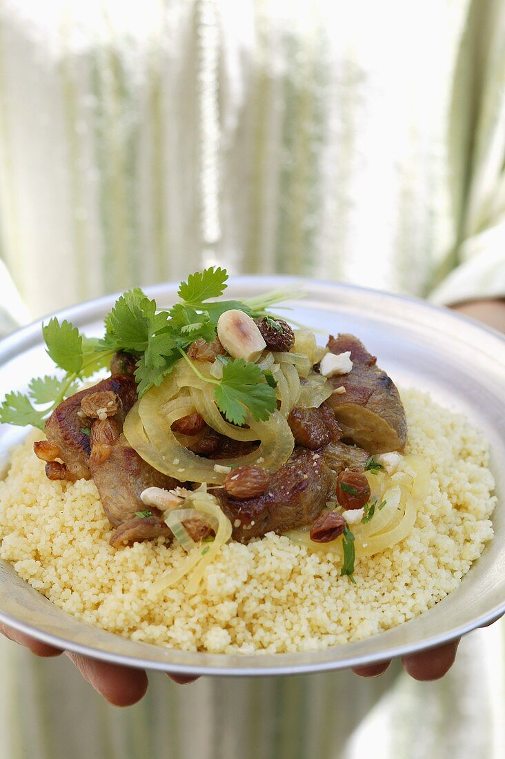 Person serving lamb ragout with almonds, raisins, couscous