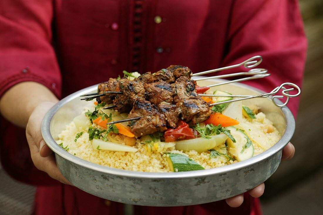Person serving kebabs with vegetables and couscous