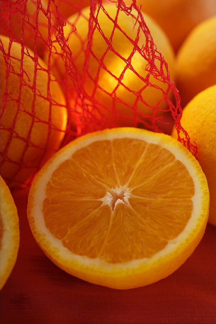 Half an orange in front of oranges in net