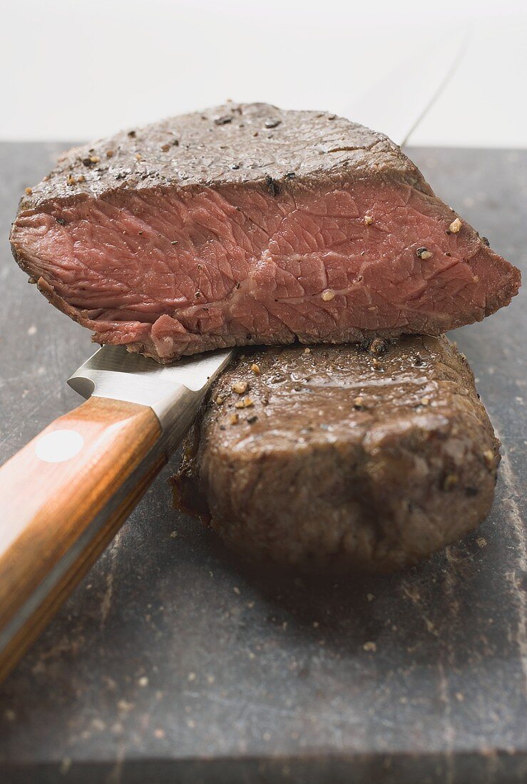 Beef steaks, one with a piece cut off, with knife