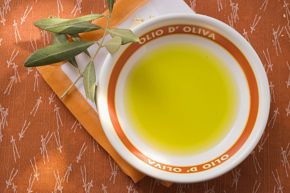 Olivenöl in Schale auf Serviette, Olivenzweig
