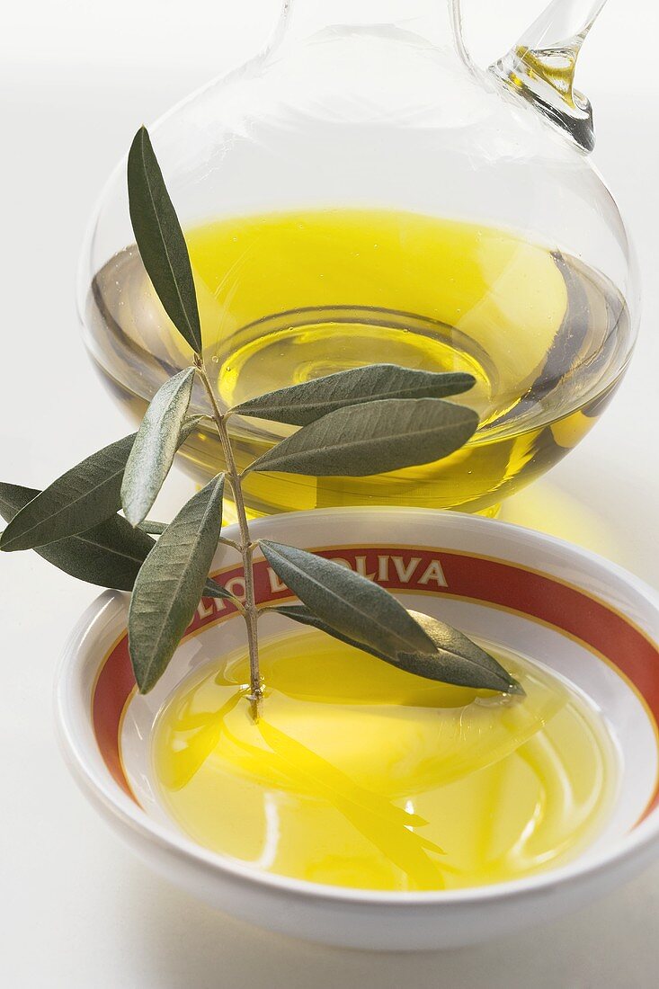 Olivenöl mit Olivenzweig in Schale vor Karaffe