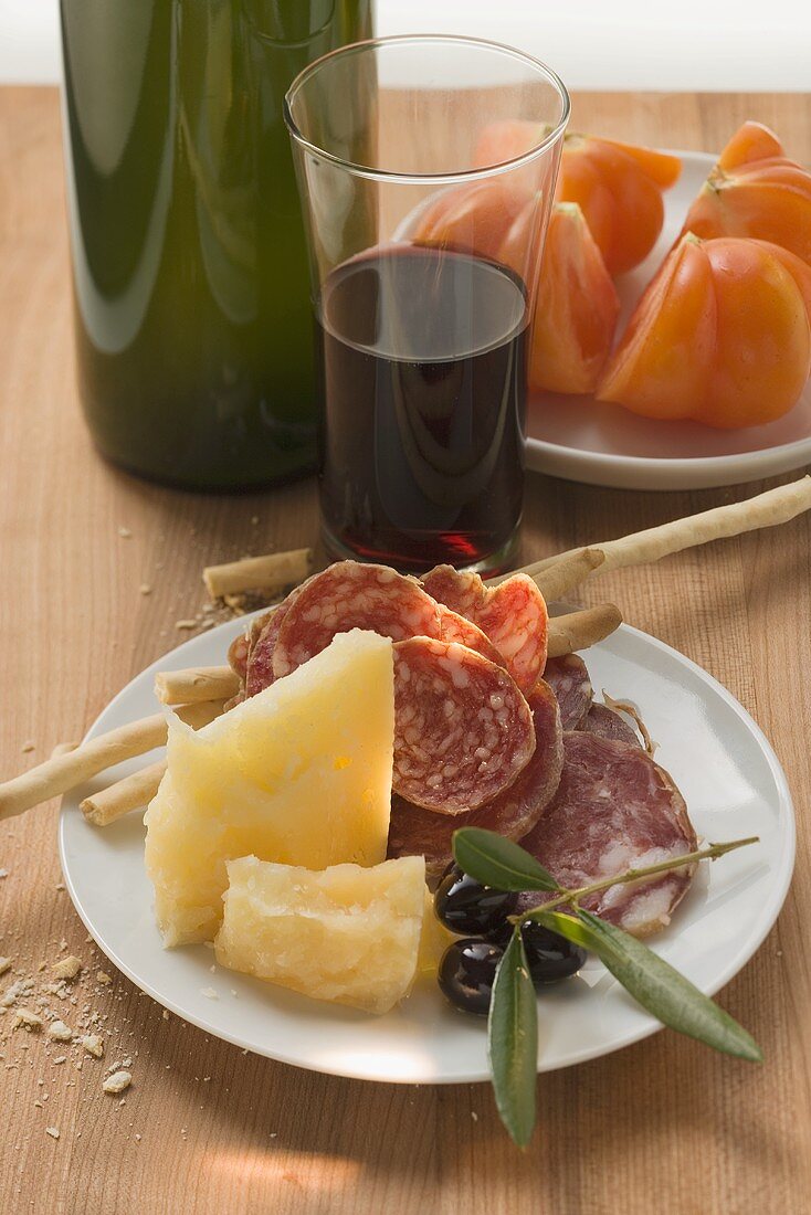 Salami, Käse, Oliven und Grissini auf Teller, Tomaten, Wein