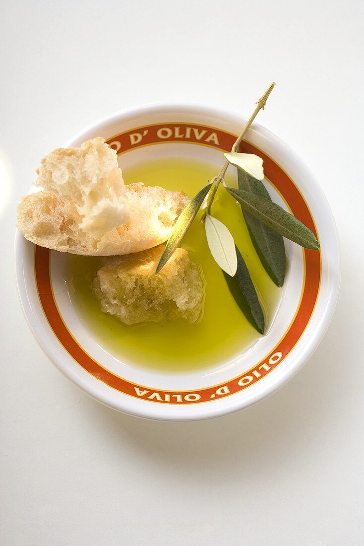Olivenöl in Schale mit Weißbrot und Olivenzweig