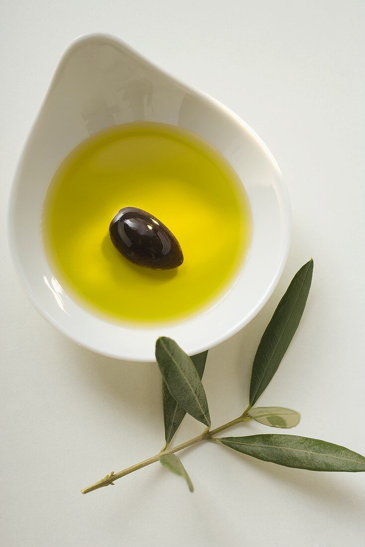 Olivenöl mit Olive in Schale, daneben Olivenzweig