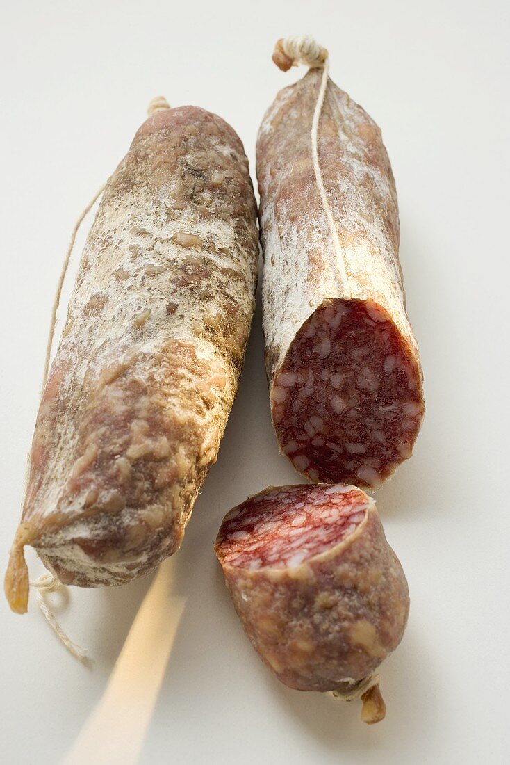 Two whole Italian salamis, one with a piece cut off