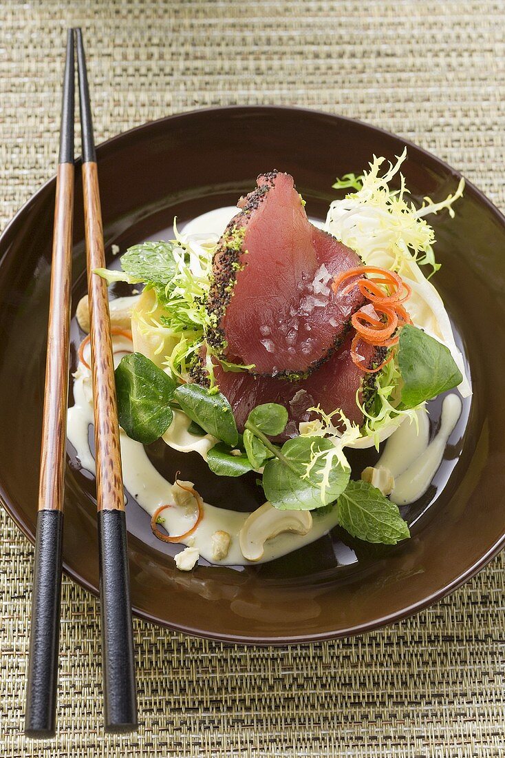 Raw tuna fillets with poppy seeds on salad in bowl