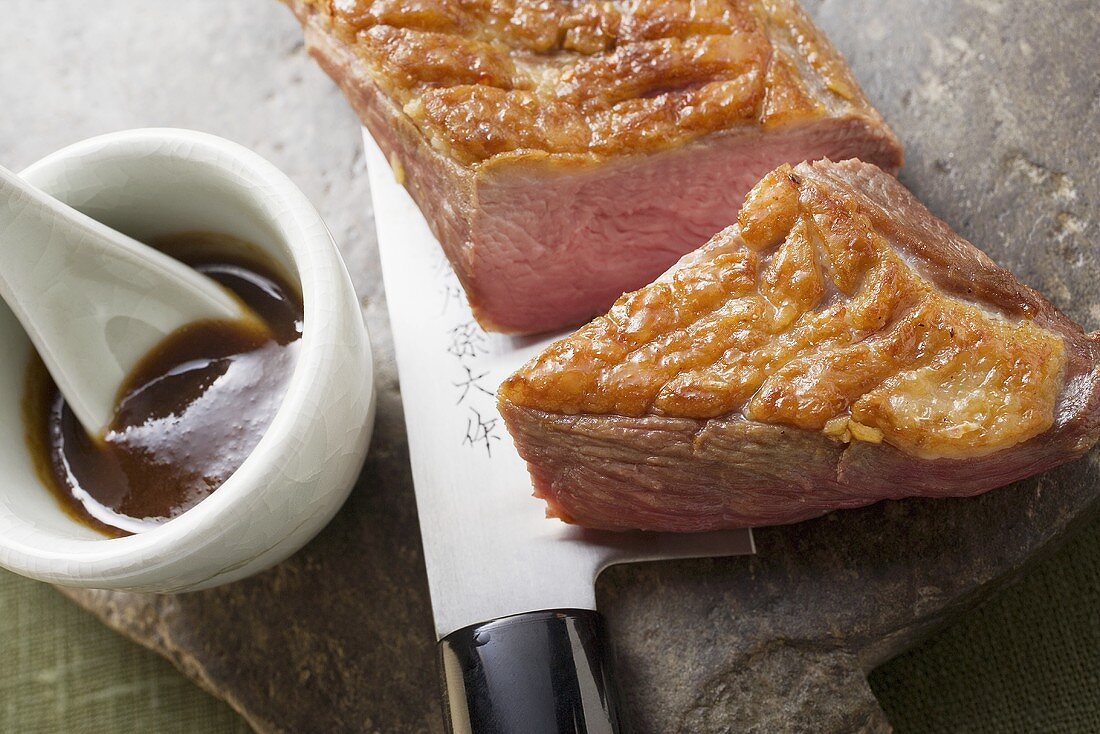 Fried duck breast, a piece cut off, on knife, soy sauce