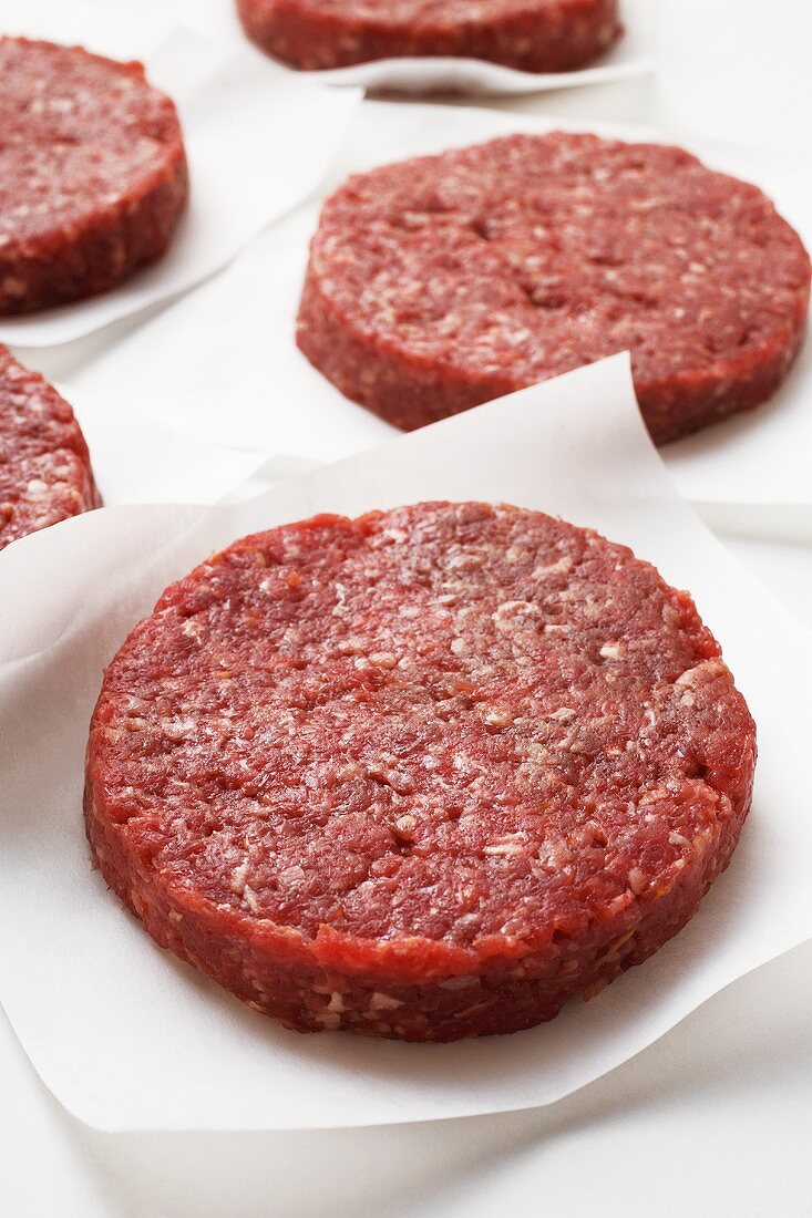 Several raw burgers on paper