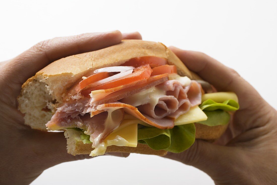 Hände halten Sub-Sandwich mit Schinken und Käse