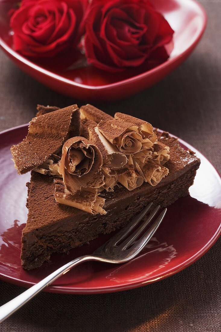 Piece of chocolate cake with chocolate curls, red roses