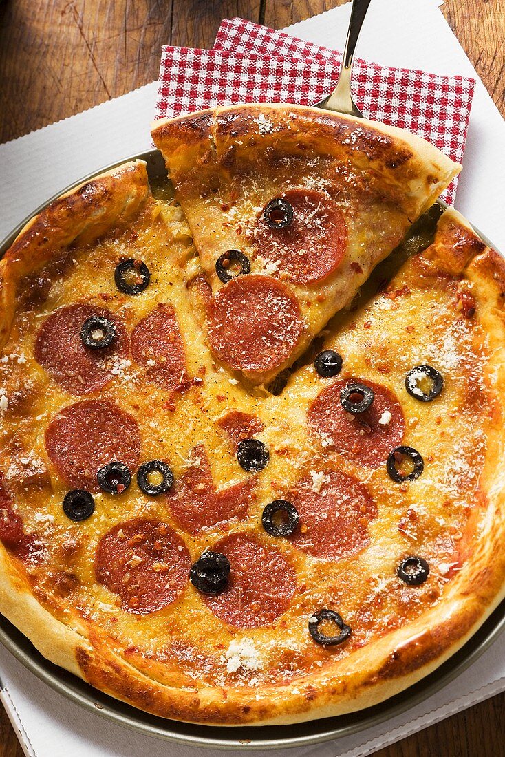 Pizza with salami, cheese and olives, a piece cut