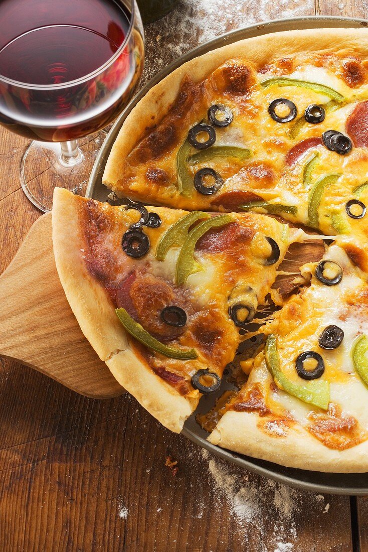 Pizza mit Käse, Salami, Paprika und Oliven, Glas Rotwein